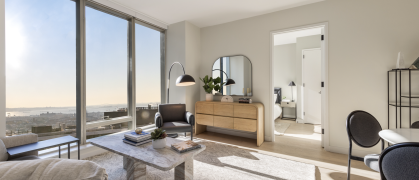 living room with sofa, white walls, & large windows looking out on NYC view